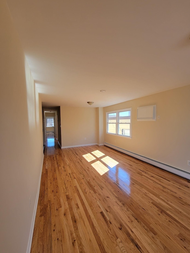 unfurnished room with a wall unit AC, light wood finished floors, baseboards, and baseboard heating