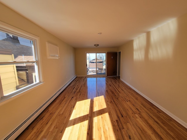 unfurnished room with baseboard heating, baseboards, and wood finished floors