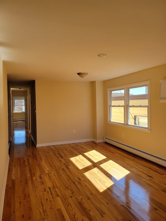 unfurnished room with a baseboard heating unit, baseboards, and wood finished floors