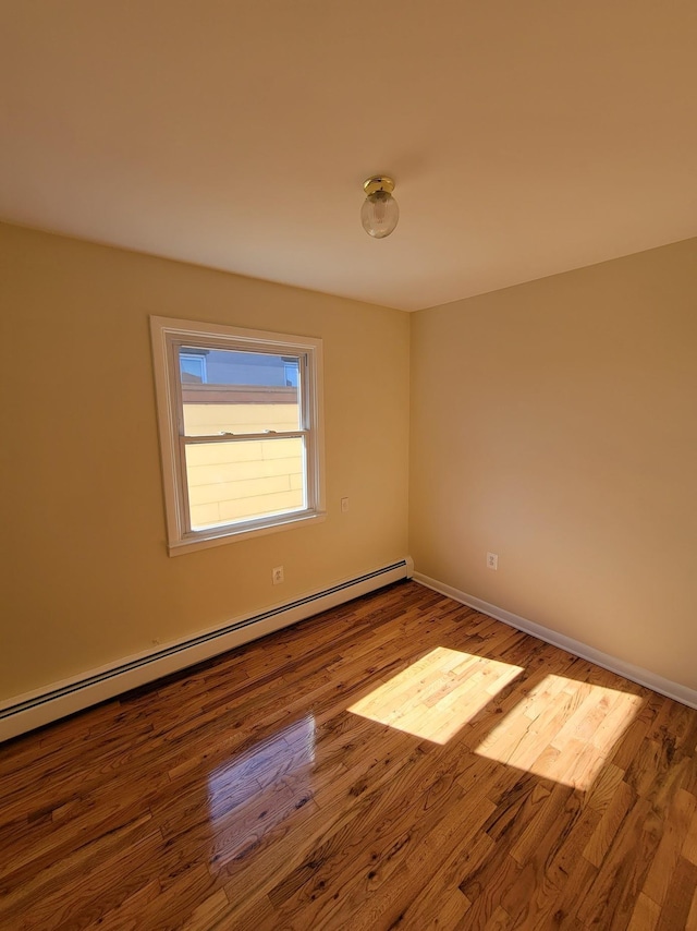 empty room featuring a baseboard heating unit, baseboards, and wood finished floors