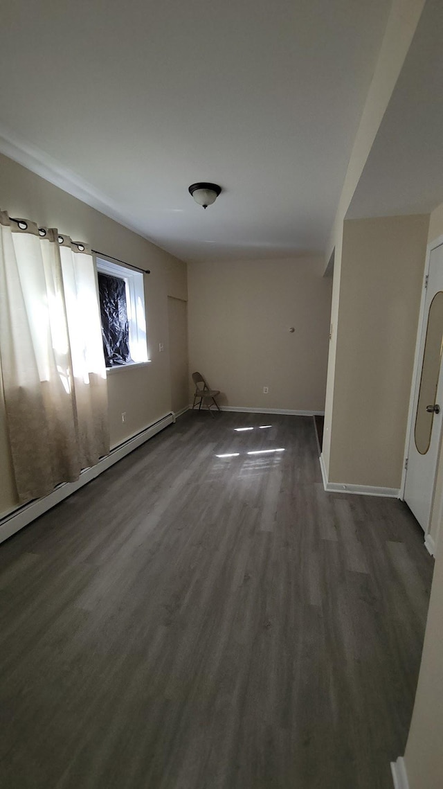 spare room with a baseboard heating unit, baseboards, and wood finished floors