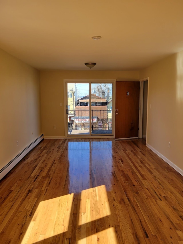 unfurnished room featuring a baseboard heating unit, wood finished floors, and baseboards