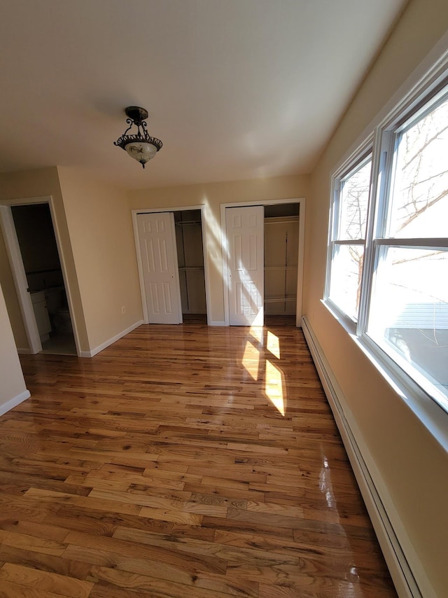 unfurnished bedroom featuring baseboards, wood finished floors, multiple closets, and a baseboard radiator