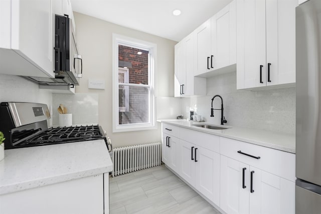 kitchen featuring stainless steel appliances, radiator heating unit, a sink, and white cabinetry