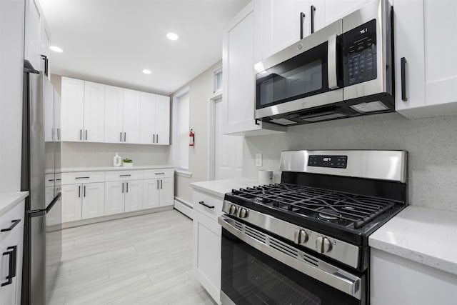 kitchen featuring a baseboard radiator, backsplash, appliances with stainless steel finishes, white cabinetry, and light stone countertops