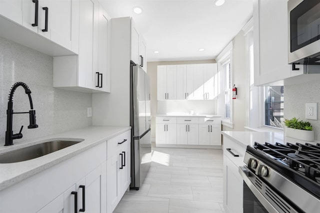 kitchen featuring stainless steel appliances, backsplash, a sink, and white cabinetry