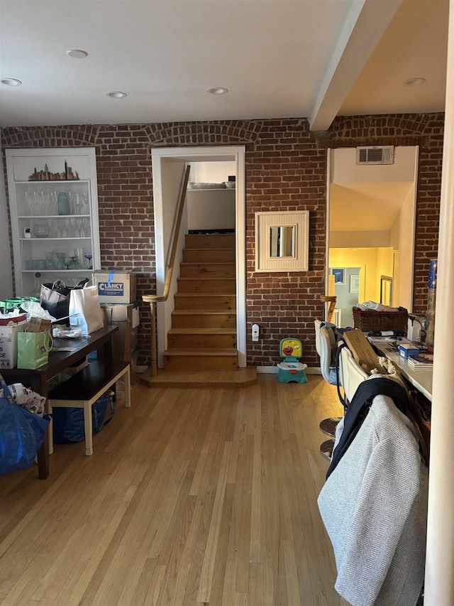 living room with beamed ceiling, brick wall, and light wood-type flooring