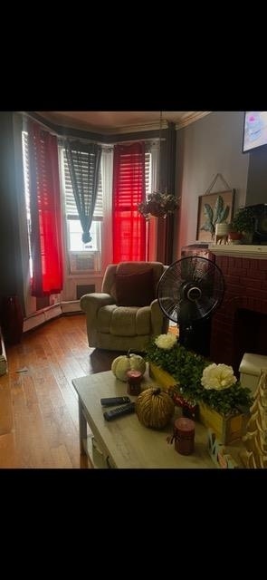 living room with baseboard heating, hardwood / wood-style flooring, and a brick fireplace