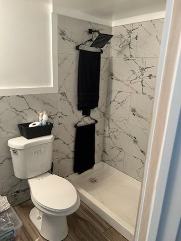 bathroom featuring tile walls, hardwood / wood-style floors, toilet, and a shower