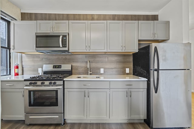 kitchen featuring appliances with stainless steel finishes, a sink, tasteful backsplash, light countertops, and dark wood finished floors