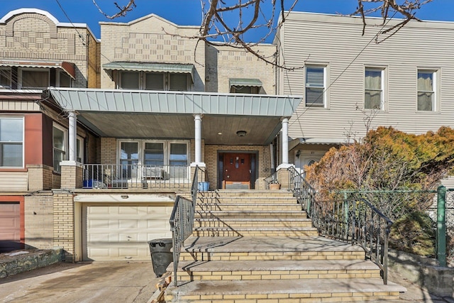 view of property featuring brick siding, an attached garage, a porch, stairs, and driveway