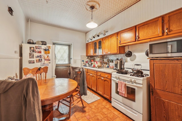 kitchen featuring backsplash, a wainscoted wall, brown cabinets, white appliances, and a sink