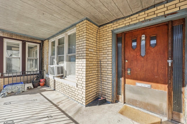 entrance to property with brick siding, covered porch, and cooling unit