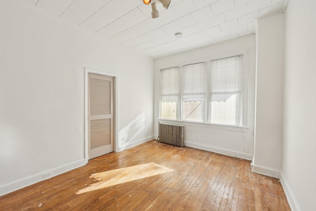 spare room featuring hardwood / wood-style floors, radiator, and baseboards