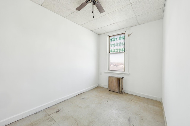 unfurnished room with a drop ceiling, ceiling fan, radiator heating unit, and baseboards