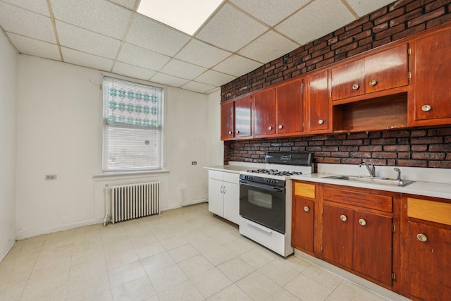 kitchen featuring gas range, radiator heating unit, light countertops, and a sink