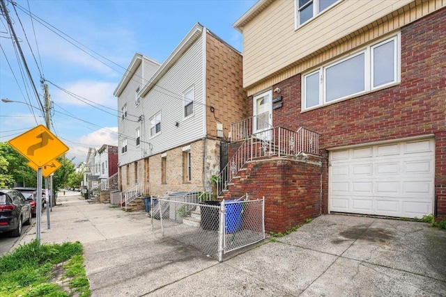 view of side of property with a garage, brick siding, driveway, and fence