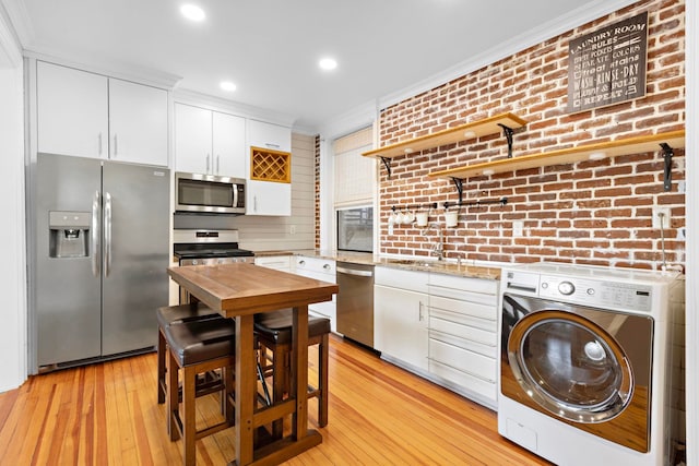 kitchen with crown molding, stainless steel appliances, white cabinets, brick wall, and washer / dryer