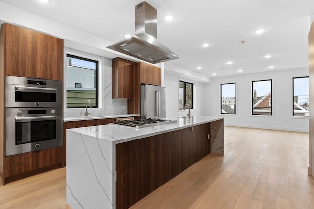 kitchen featuring a spacious island, sink, light stone counters, appliances with stainless steel finishes, and island exhaust hood