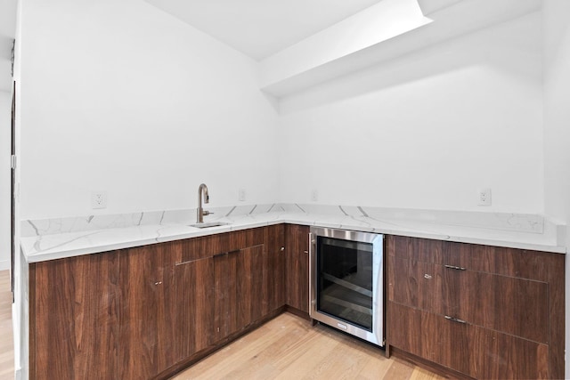 kitchen featuring wine cooler, dark brown cabinetry, sink, light stone counters, and light wood-type flooring