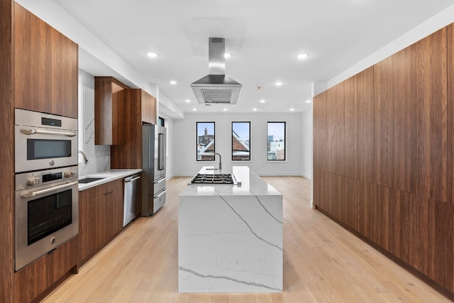 kitchen with sink, island range hood, a kitchen island, stainless steel appliances, and light stone countertops