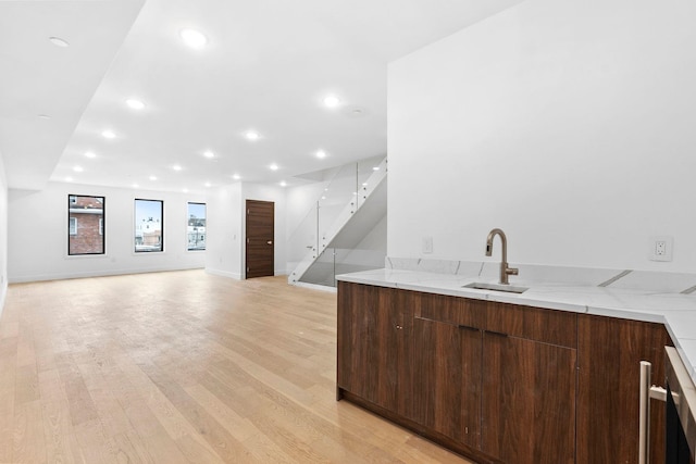 bar with light stone countertops, sink, dark brown cabinets, and light hardwood / wood-style flooring