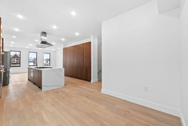 kitchen with island range hood, stainless steel refrigerator, a kitchen island, light stone countertops, and light hardwood / wood-style floors