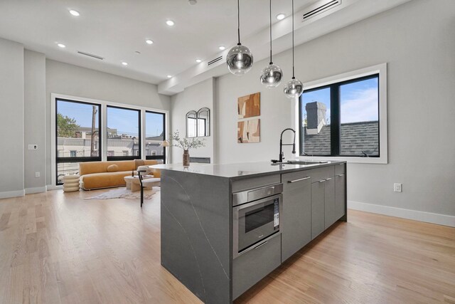 371 New York Ave Unit 2, Jersey City, NJ 07307 - kitchen featuring modern cabinets, gray cabinetry, an island with sink, stainless steel microwave, and light wood-type flooring