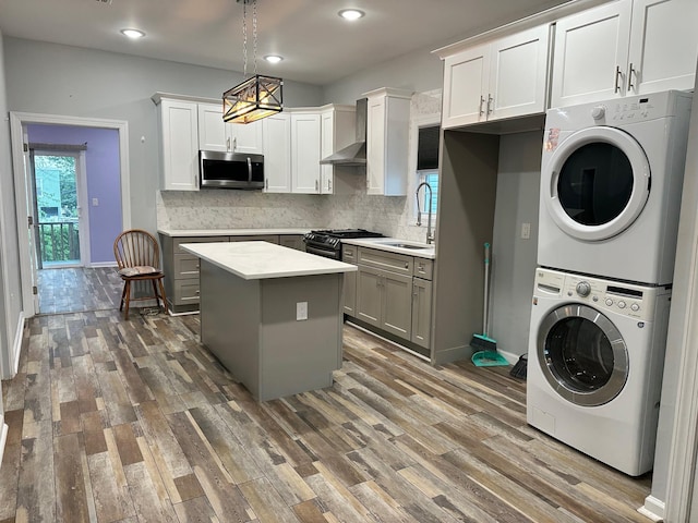 29 W 26th St, Bayonne, NJ 07002 - kitchen featuring stainless steel microwave, stacked washing machine and dryer, wall chimney exhaust hood, range with gas cooktop, and gray cabinetry