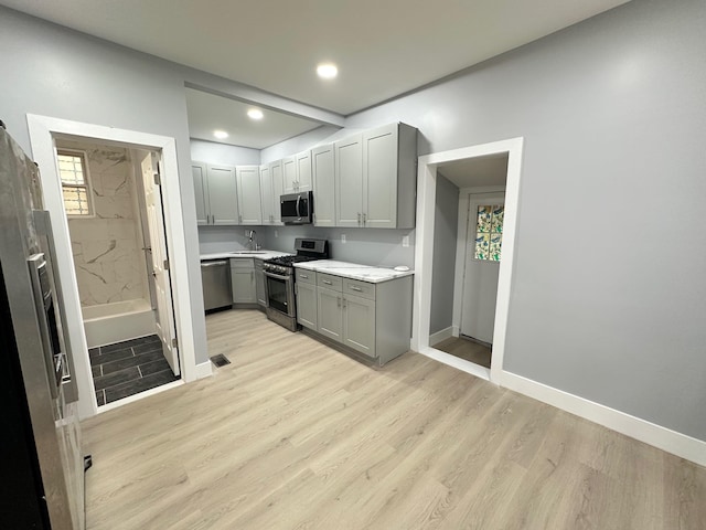 29 W 26th St, Bayonne, NJ 07002 - kitchen with stainless steel appliances, gray cabinetry, a sink, baseboards, and light wood-style floors