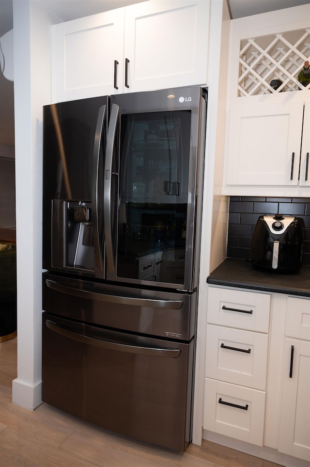 interior details with white cabinetry, decorative backsplash, stainless steel fridge, and light wood-type flooring