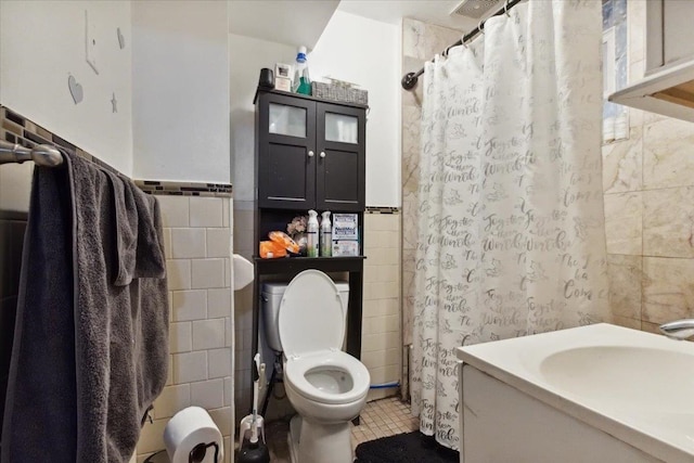 bathroom with curtained shower, vanity, tile patterned floors, toilet, and tile walls