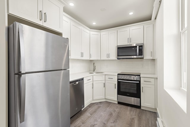 235 Monroe St Unit 10, Hoboken, NJ 07030 - kitchen with appliances with stainless steel finishes, light countertops, light wood-style floors, white cabinetry, and decorative backsplash