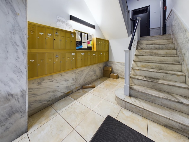 stairway featuring tile patterned floors, mail boxes, lofted ceiling, and tile walls