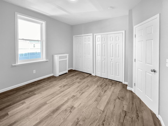 unfurnished bedroom featuring multiple closets, radiator heating unit, and light wood-type flooring