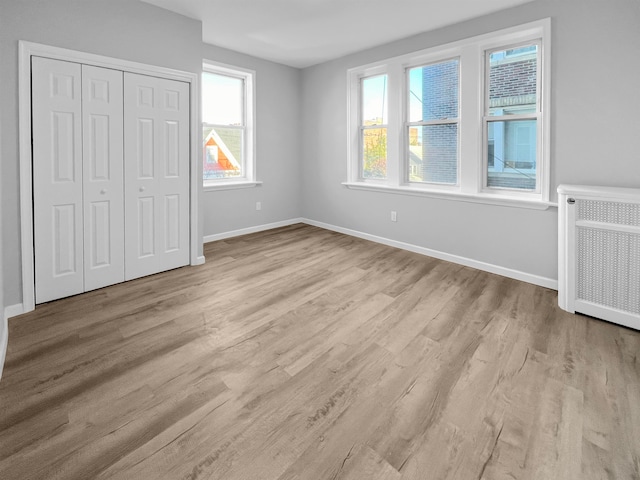 unfurnished bedroom featuring a closet, light wood-type flooring, radiator heating unit, and multiple windows