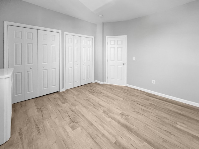 unfurnished bedroom with two closets and light hardwood / wood-style flooring