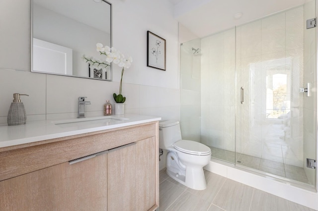 bathroom with toilet, tile patterned floors, vanity, tile walls, and a shower with shower door