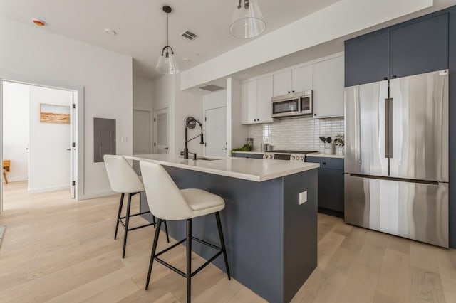 kitchen featuring decorative light fixtures, stainless steel appliances, an island with sink, white cabinetry, and sink