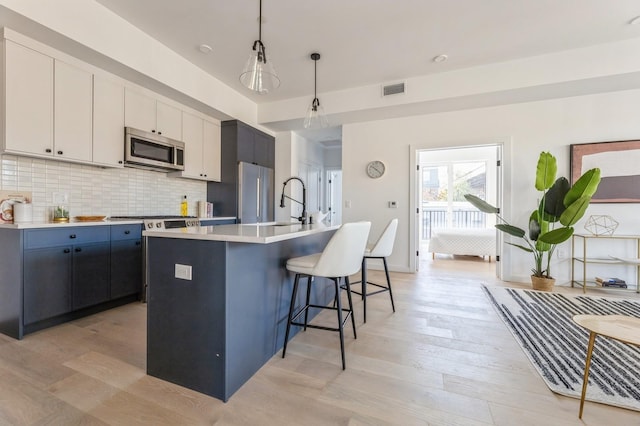 kitchen with hanging light fixtures, stainless steel appliances, a center island with sink, decorative backsplash, and white cabinets