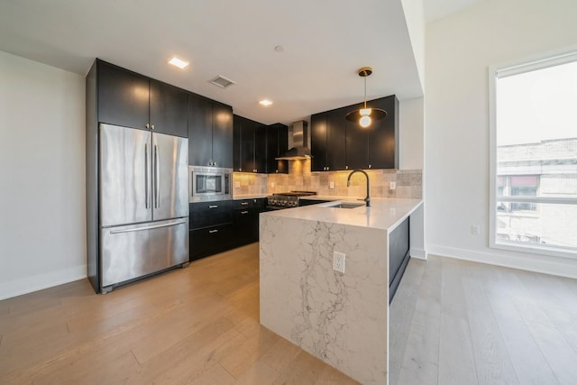 202 Merseles St Unit 503, Jersey City, NJ 07302 - kitchen with appliances with stainless steel finishes, wall chimney range hood, dark cabinets, a peninsula, and light wood-style flooring