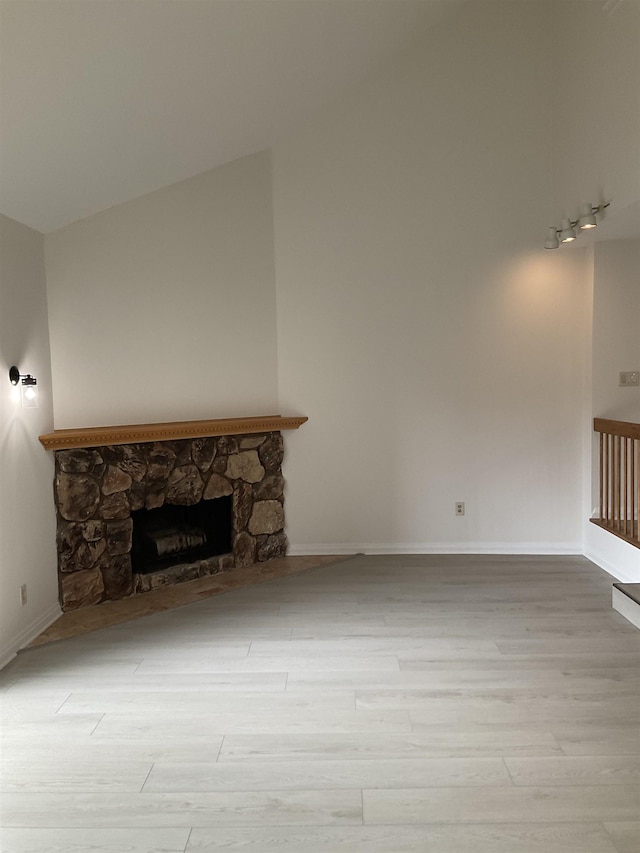 unfurnished living room with vaulted ceiling, light wood-type flooring, a fireplace, and track lighting