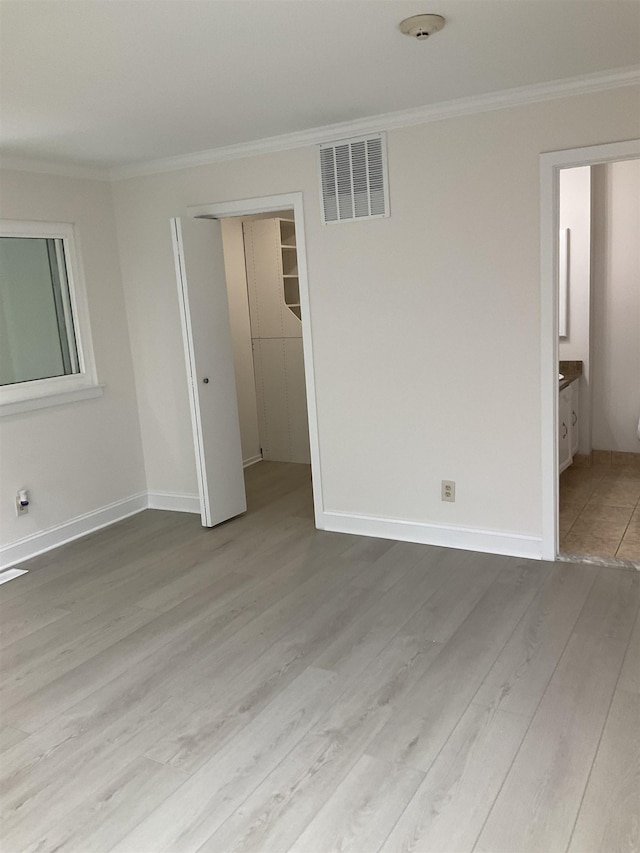 unfurnished bedroom with hardwood / wood-style floors, connected bathroom, a closet, and ornamental molding