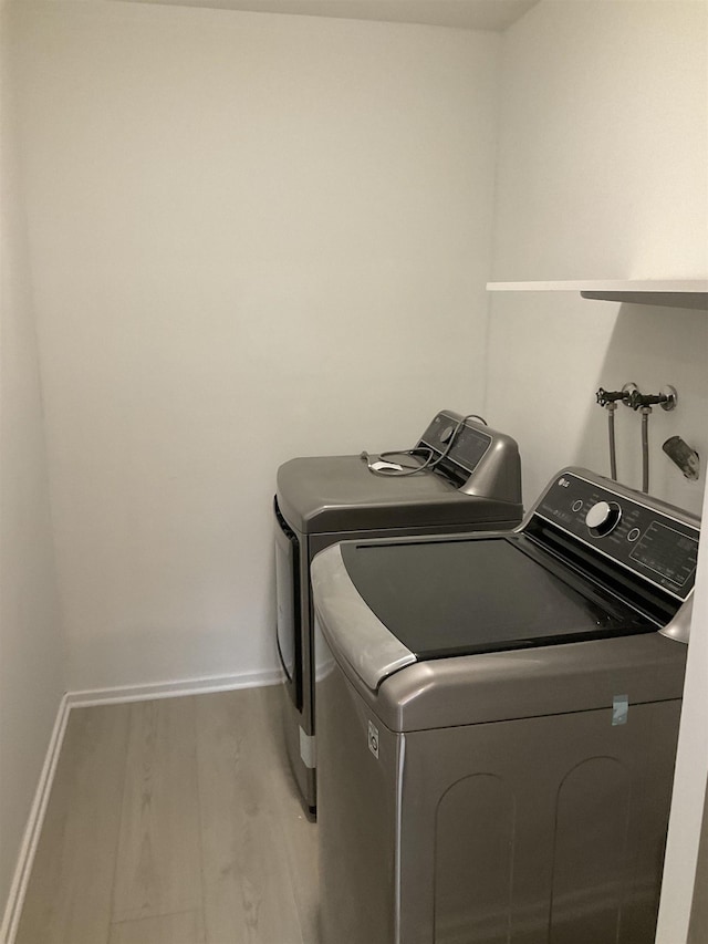 clothes washing area with washing machine and dryer and light hardwood / wood-style floors