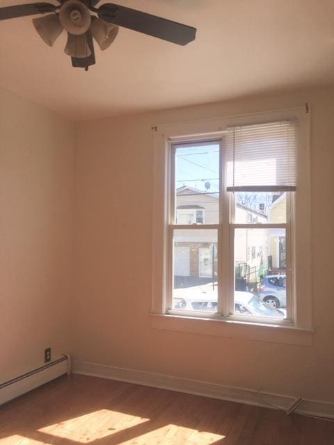 unfurnished room with ceiling fan, hardwood / wood-style floors, and a baseboard heating unit