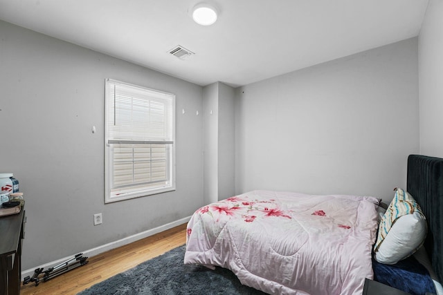 bedroom with wood finished floors, visible vents, and baseboards