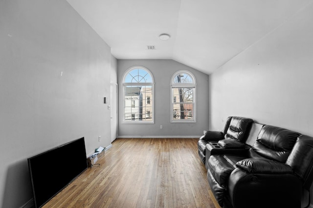 living room with light wood-style flooring, visible vents, vaulted ceiling, and baseboards