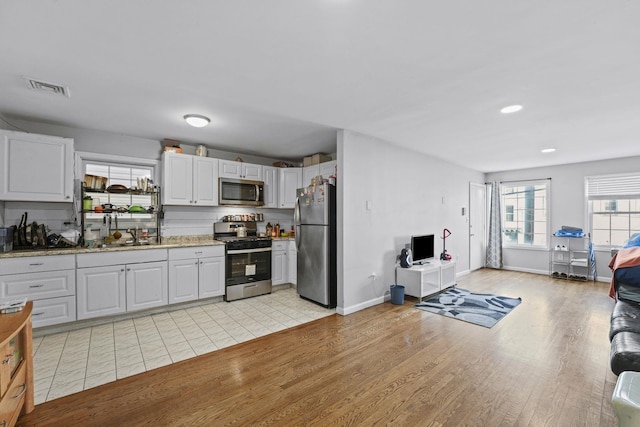 kitchen with stainless steel appliances, a sink, visible vents, white cabinetry, and light wood-style floors