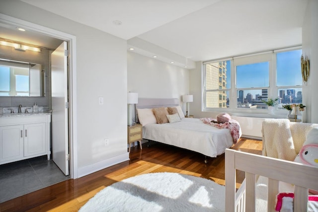 bedroom with a view of city, wood finished floors, multiple windows, and a sink