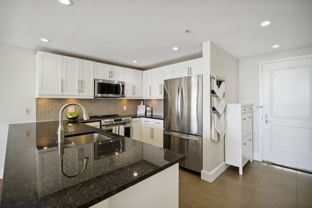 kitchen featuring a peninsula, appliances with stainless steel finishes, white cabinets, and dark stone countertops